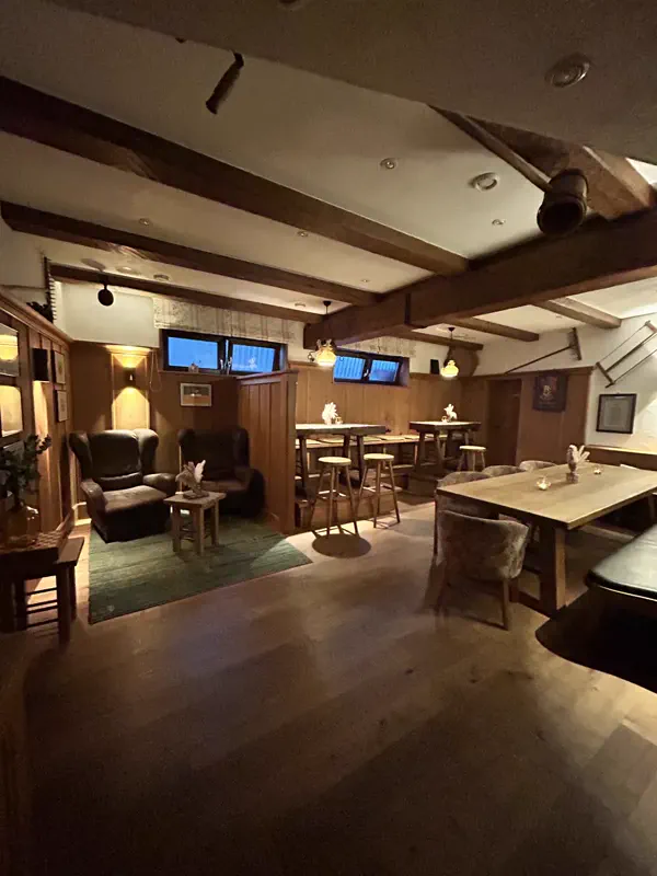 Lounge mit Ledersesseln und Stehtischen unter Holzbalken